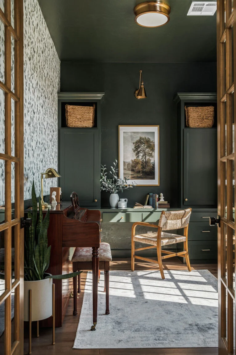 Sunlit study with deep olive painted walls, wood furniture, and brass details
