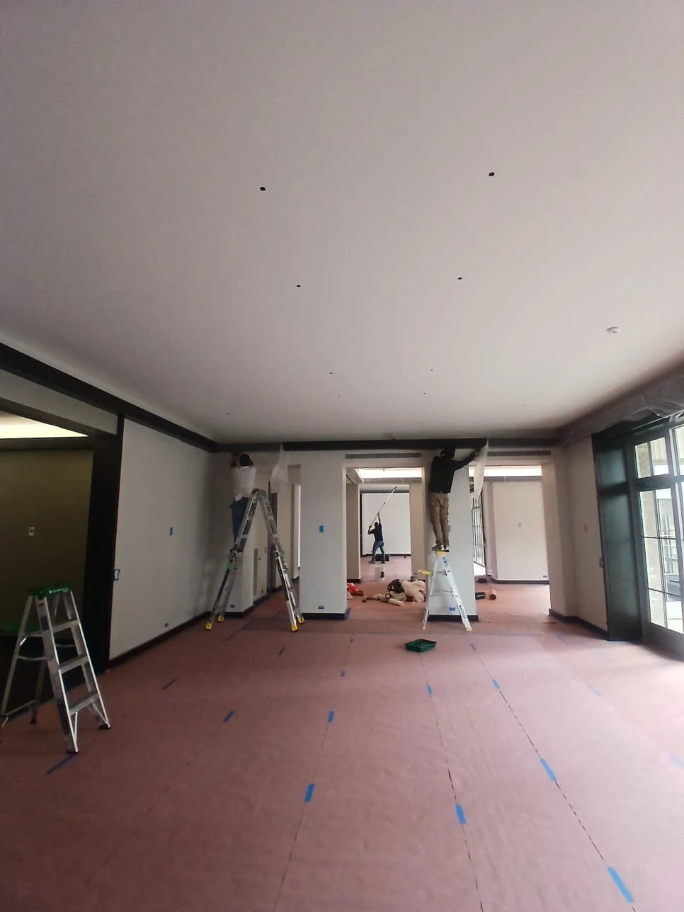 Painters work across the room with flooring covered beneath their work areas.